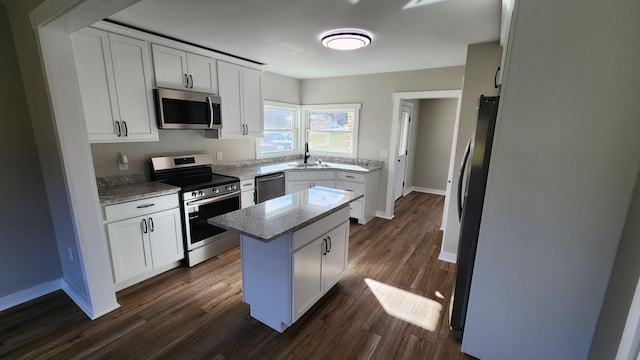 kitchen featuring dark wood-type flooring, a kitchen island, light stone counters, white cabinets, and appliances with stainless steel finishes