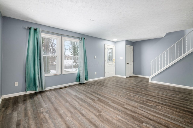 unfurnished living room with visible vents, a textured ceiling, wood finished floors, baseboards, and stairs