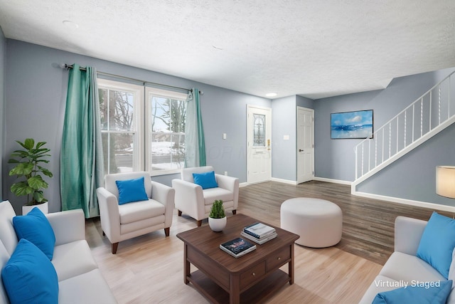 living room with stairs, light wood finished floors, a textured ceiling, and baseboards