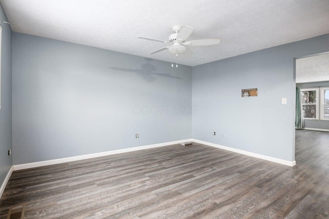 empty room featuring a textured ceiling, a ceiling fan, visible vents, baseboards, and dark wood finished floors