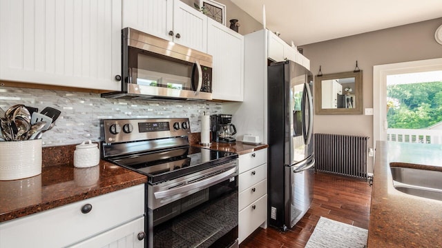 kitchen featuring white cabinetry, radiator heating unit, stainless steel appliances, dark hardwood / wood-style flooring, and dark stone counters