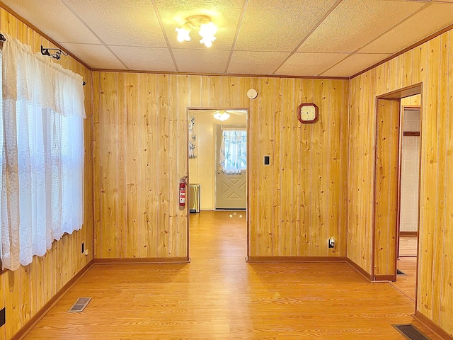 empty room featuring hardwood / wood-style flooring, a drop ceiling, and wooden walls