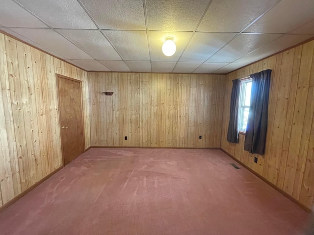 unfurnished room with a paneled ceiling, wood walls, and carpet floors