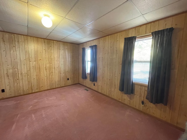 carpeted empty room featuring wooden walls and a drop ceiling