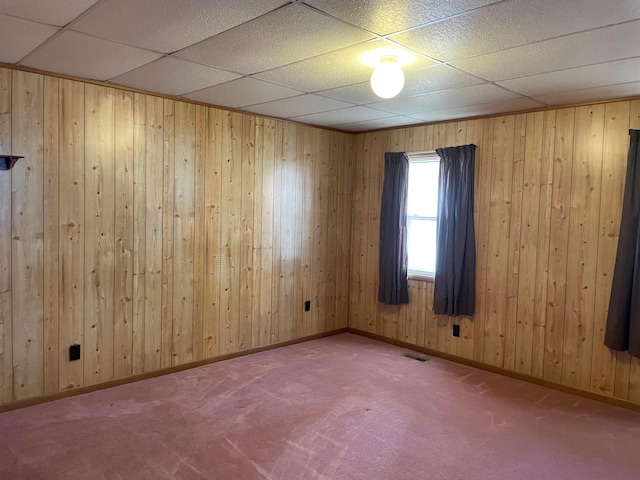 unfurnished room featuring a paneled ceiling, wood walls, and carpet