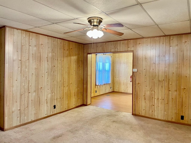 unfurnished room with carpet flooring, wood walls, and ceiling fan