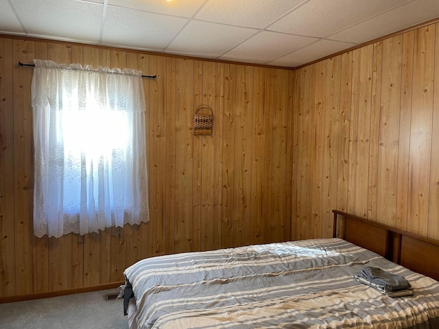 bedroom with wood walls, a drop ceiling, and carpet floors