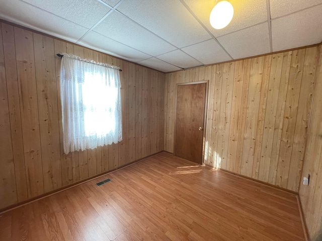 unfurnished room with hardwood / wood-style flooring, a paneled ceiling, and wooden walls