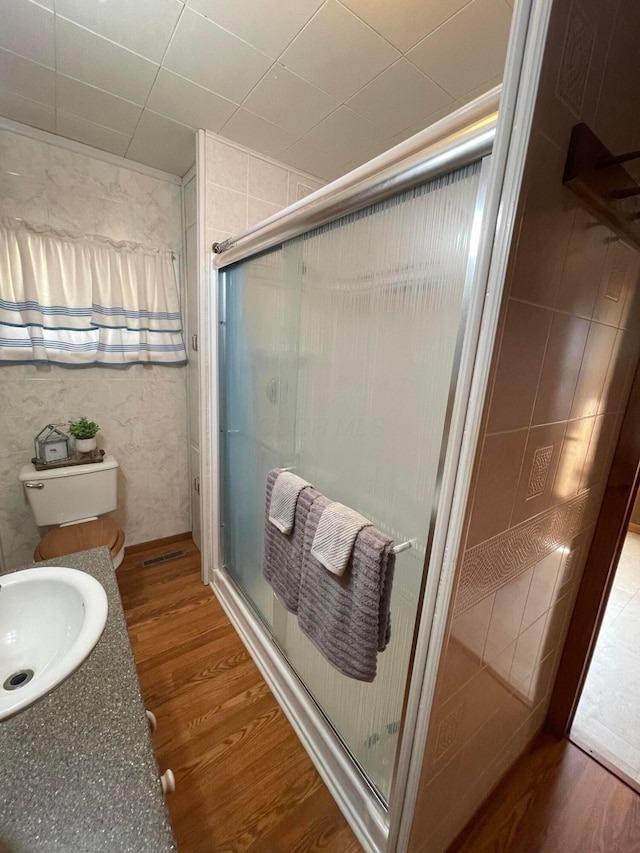 bathroom featuring wood-type flooring, an enclosed shower, toilet, vanity, and tile walls