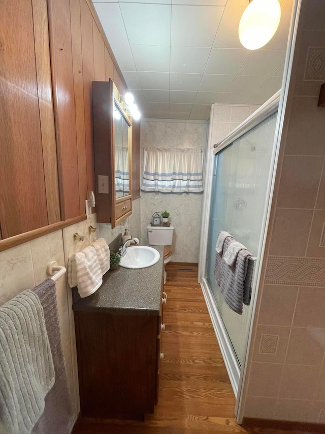 bathroom with vanity, a shower with door, hardwood / wood-style flooring, toilet, and tile walls