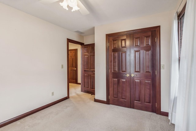 unfurnished bedroom with a closet, light colored carpet, and ceiling fan