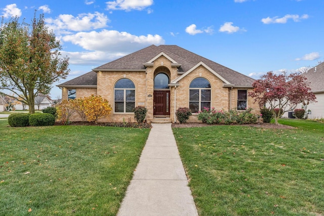 view of front of home featuring brick siding, a front yard, and a shingled roof