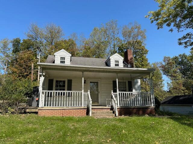 view of front of home with a porch, a chimney, and a front lawn