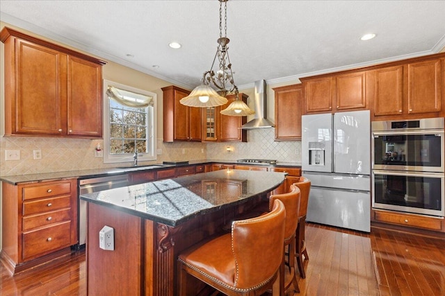 kitchen featuring ornamental molding, wall chimney exhaust hood, stainless steel appliances, a center island, and a breakfast bar area