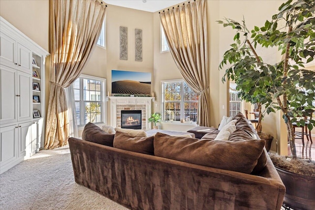 living room with carpet, a healthy amount of sunlight, a towering ceiling, and a tiled fireplace