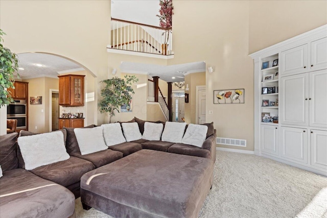 carpeted living room with built in shelves, crown molding, and a high ceiling