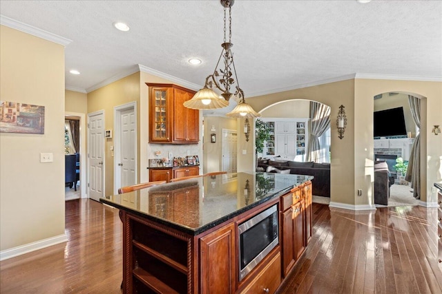 kitchen featuring stainless steel microwave, dark stone counters, dark hardwood / wood-style floors, decorative light fixtures, and a kitchen island