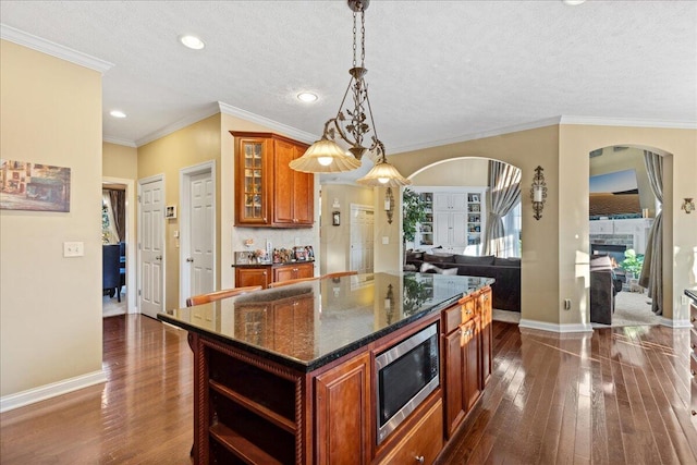 kitchen with stainless steel microwave, a center island, dark hardwood / wood-style floors, dark stone counters, and pendant lighting