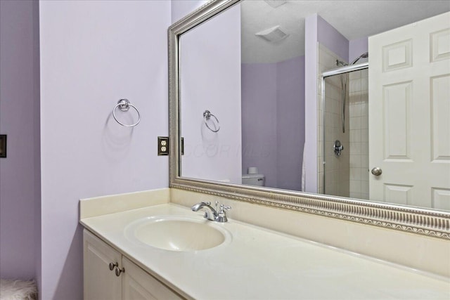 bathroom with a shower with door, vanity, a textured ceiling, and toilet