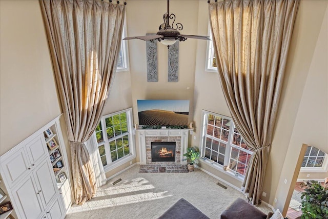 carpeted living room featuring ceiling fan, a healthy amount of sunlight, and a towering ceiling