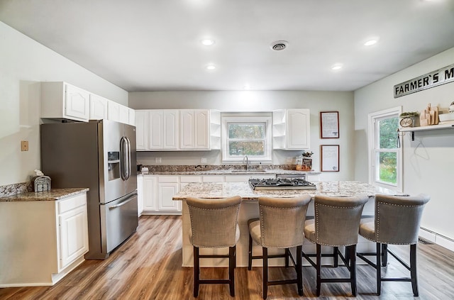 kitchen with white cabinets, stainless steel refrigerator with ice dispenser, light hardwood / wood-style floors, and a kitchen island