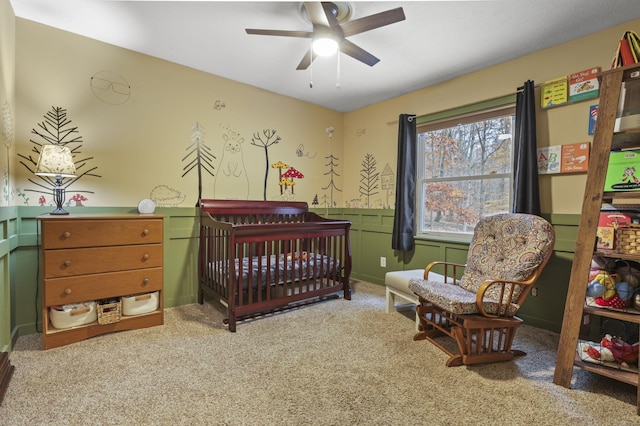 carpeted bedroom featuring a crib and ceiling fan