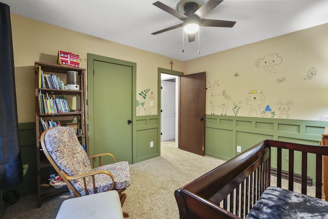 carpeted bedroom featuring ceiling fan and a crib