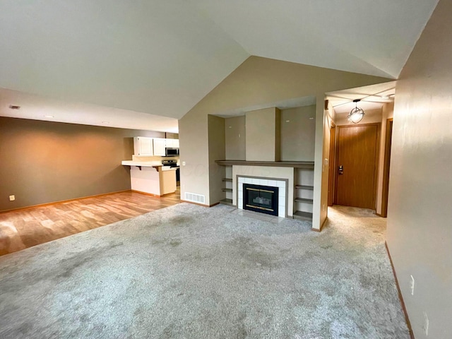 unfurnished living room featuring light carpet, baseboards, visible vents, lofted ceiling, and a fireplace