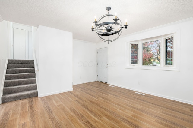 unfurnished room featuring an inviting chandelier, ornamental molding, a textured ceiling, and light hardwood / wood-style flooring