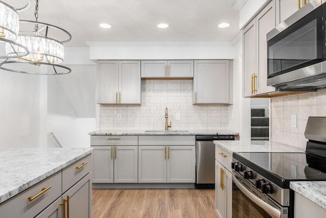 kitchen with sink, gray cabinets, light stone countertops, a notable chandelier, and stainless steel appliances