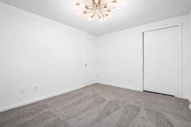 carpeted spare room with a textured ceiling and a chandelier