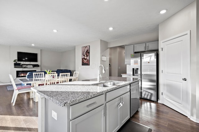 kitchen with appliances with stainless steel finishes, light stone counters, sink, dark hardwood / wood-style floors, and an island with sink