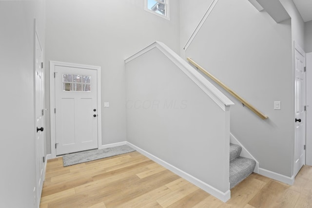 entryway featuring light wood-type flooring, baseboards, a towering ceiling, and stairway