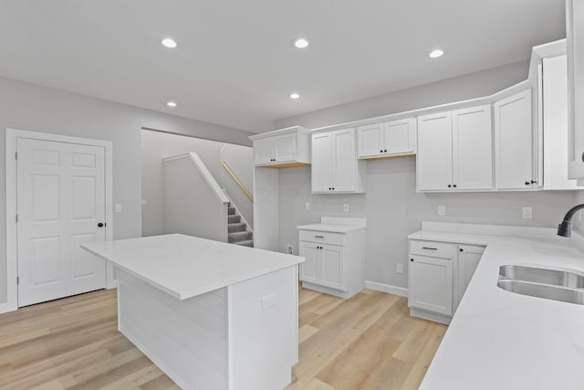 kitchen featuring a kitchen island, white cabinetry, a sink, and light wood finished floors