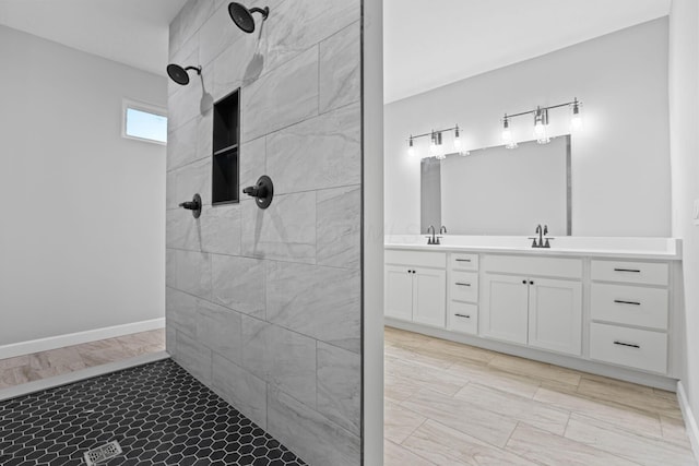 bathroom featuring tiled shower, a sink, baseboards, and double vanity