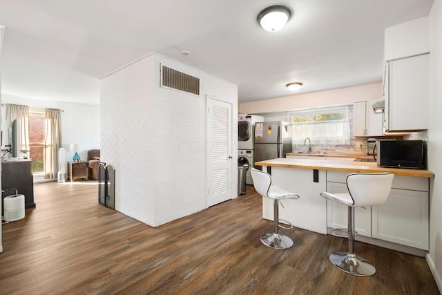 kitchen with wooden counters, sink, stacked washing maching and dryer, a kitchen bar, and wood-type flooring