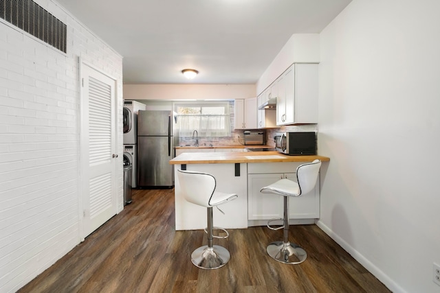 kitchen with a breakfast bar, white cabinets, stacked washing maching and dryer, butcher block counters, and stainless steel appliances