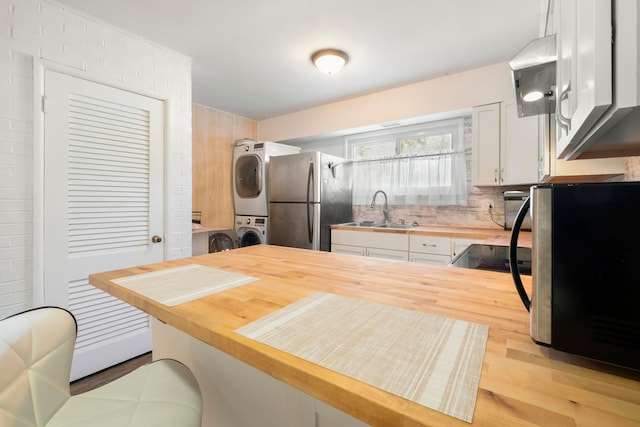 kitchen with stainless steel appliances, sink, light hardwood / wood-style flooring, stacked washer and dryer, and white cabinetry