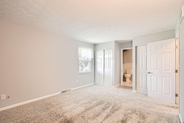 unfurnished bedroom featuring a textured ceiling, ensuite bathroom, and light carpet