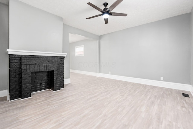 unfurnished living room featuring a textured ceiling, light hardwood / wood-style flooring, a brick fireplace, and ceiling fan