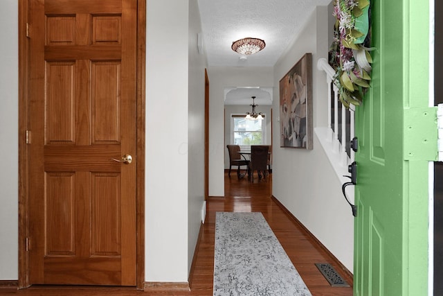 foyer entrance with an inviting chandelier, dark wood-style flooring, baseboards, and visible vents
