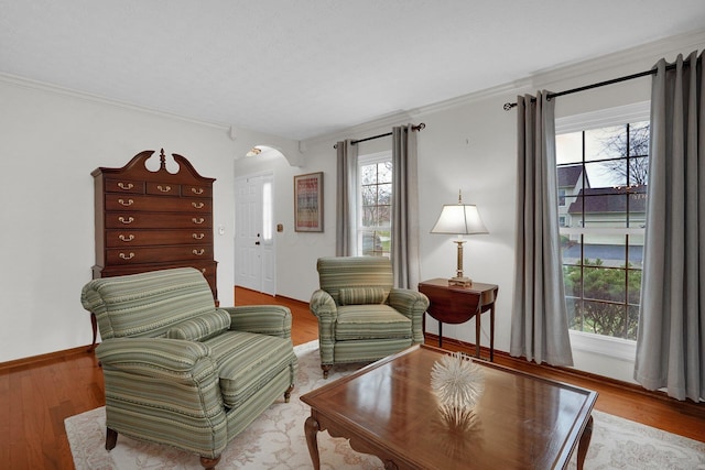 living area with arched walkways, baseboards, wood finished floors, and crown molding