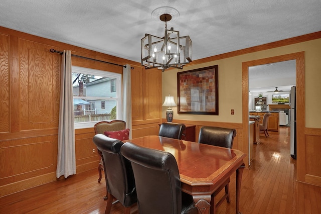dining room featuring crown molding, light wood-type flooring, a chandelier, a textured ceiling, and wainscoting