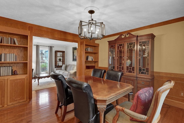 dining area with crown molding, wooden walls, wood finished floors, built in features, and a notable chandelier