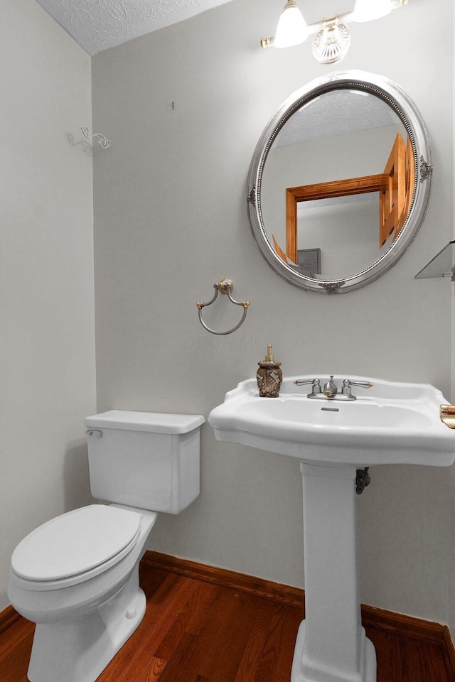 bathroom with toilet, a sink, wood finished floors, a textured ceiling, and baseboards