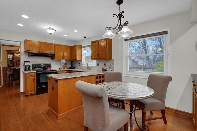 kitchen with hardwood / wood-style flooring, brown cabinets, under cabinet range hood, a sink, and electric range