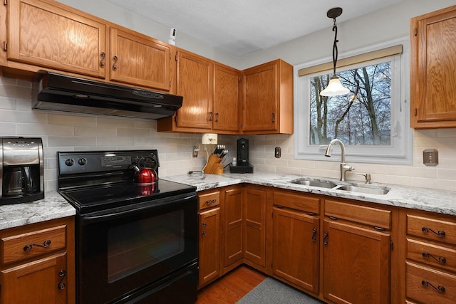 kitchen with a sink, black range with electric cooktop, under cabinet range hood, and brown cabinets