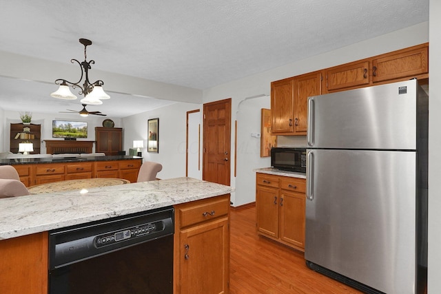 kitchen featuring light stone countertops, brown cabinets, light wood-type flooring, hanging light fixtures, and black appliances