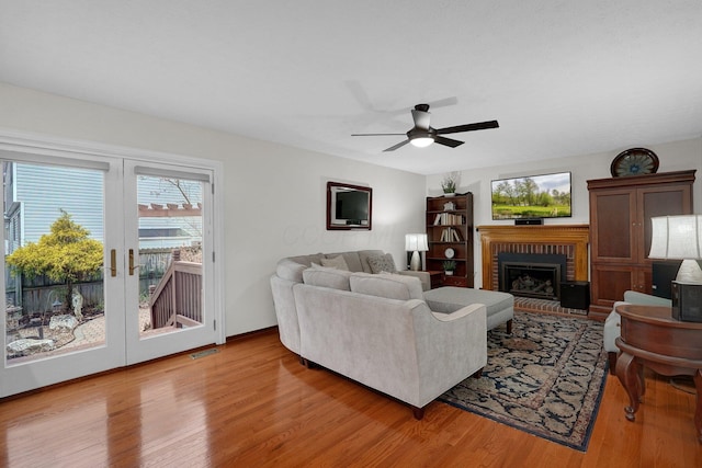 living area with a ceiling fan, visible vents, light wood-type flooring, and a brick fireplace
