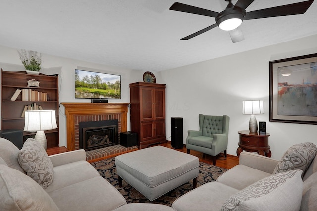 living area with wood finished floors, a ceiling fan, and a brick fireplace